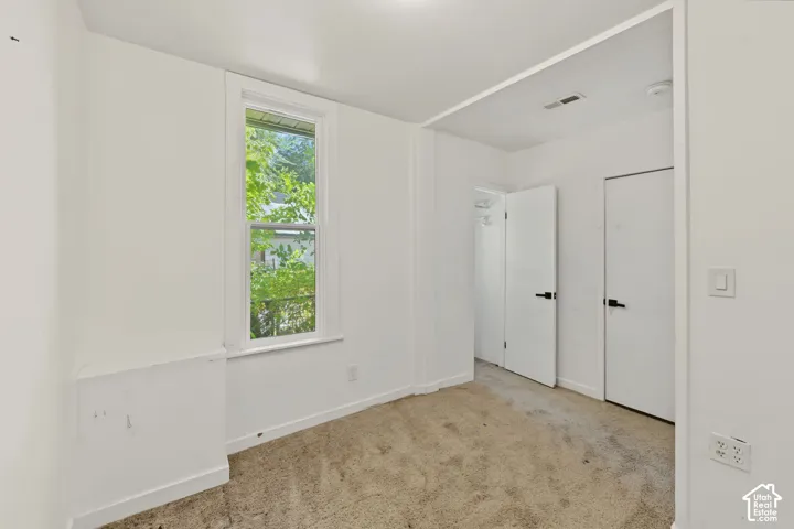 Room featuring neutral-toned carpeting, white walls, a single-hung window with natural light, and dual interior doors with matte black hardware