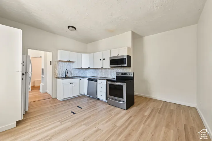 Kitchen featuring white cabinetry, wood-finish flooring, a hexagonal patterned backsplash, stainless steel appliances, and a matte black faucet