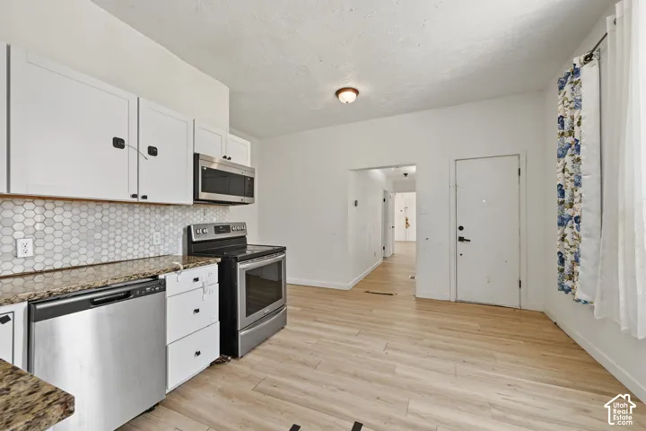 Kitchen featuring white cabinetry, stone-finish countertops, stainless steel appliances, a hexagon tile backsplash, and wood-finish flooring