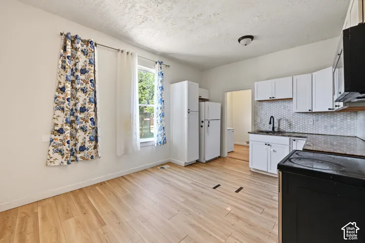 Kitchen featuring white shaker-style cabinetry, wood-finish flooring, a hexagonal tile backsplash, and a matte black faucet