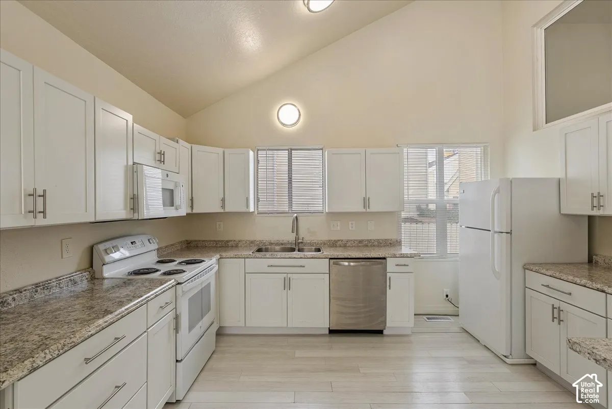 Kitchen featuring vaulted ceilings, white shaker-style cabinetry, stone-finish countertops, stainless steel dishwasher, and wood-finish flooring