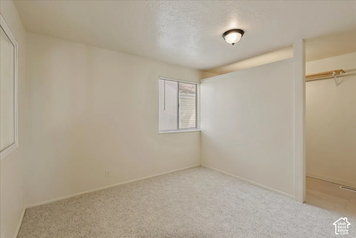 Neutral-toned wall-to-wall carpeting, window with blinds, ceiling-mounted light fixture, and built-in closet storage