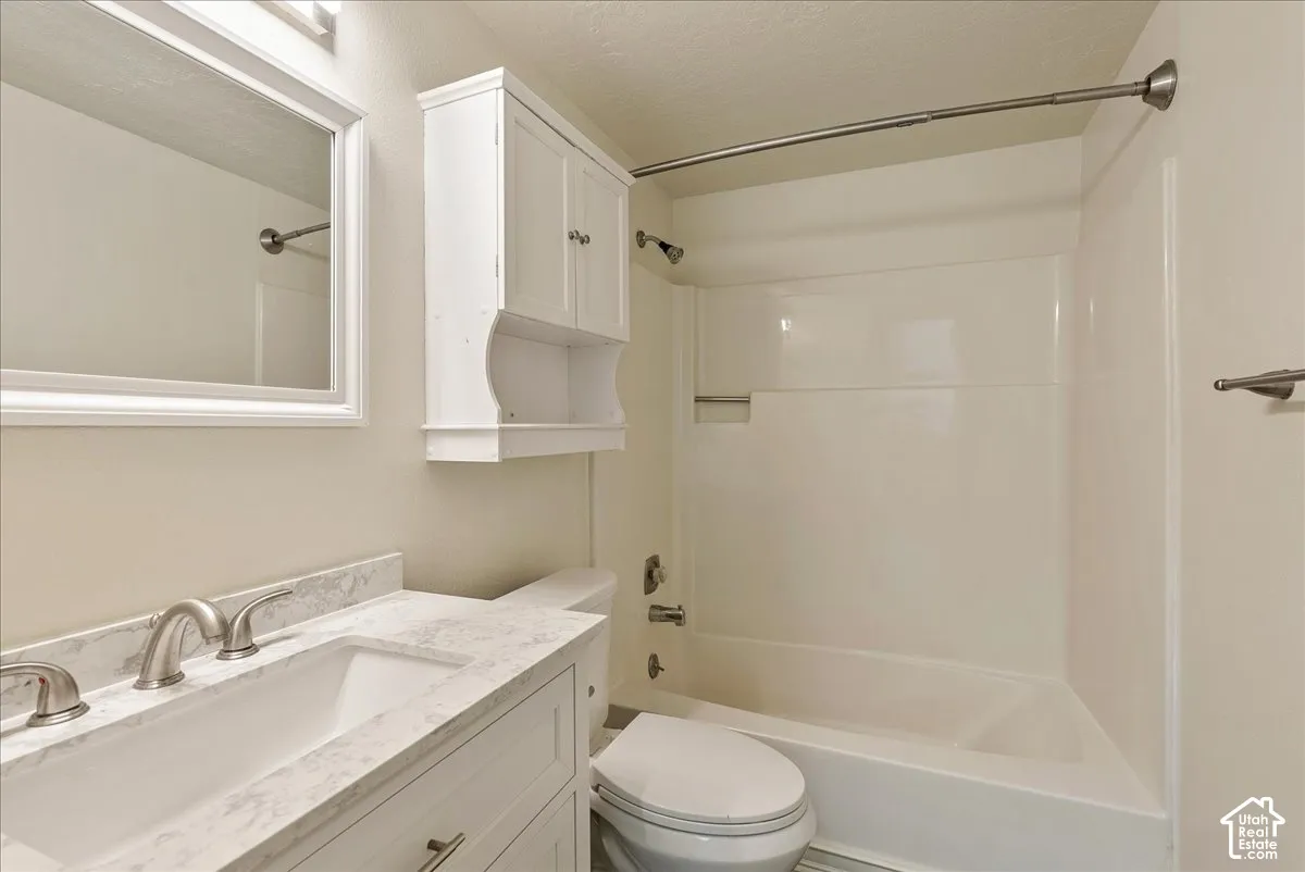 Bathroom featuring a vanity with a white countertop and undermount sink, wall-mounted storage cabinet, framed mirror, and a tub-shower combination with a surround