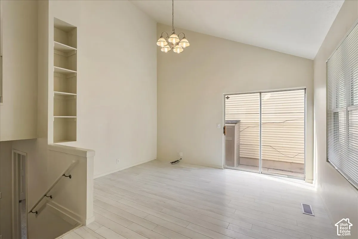 Vaulted ceilings, light-tone wood-finish flooring, built-in wall shelving, multi-bulb chandelier, and sliding glass door