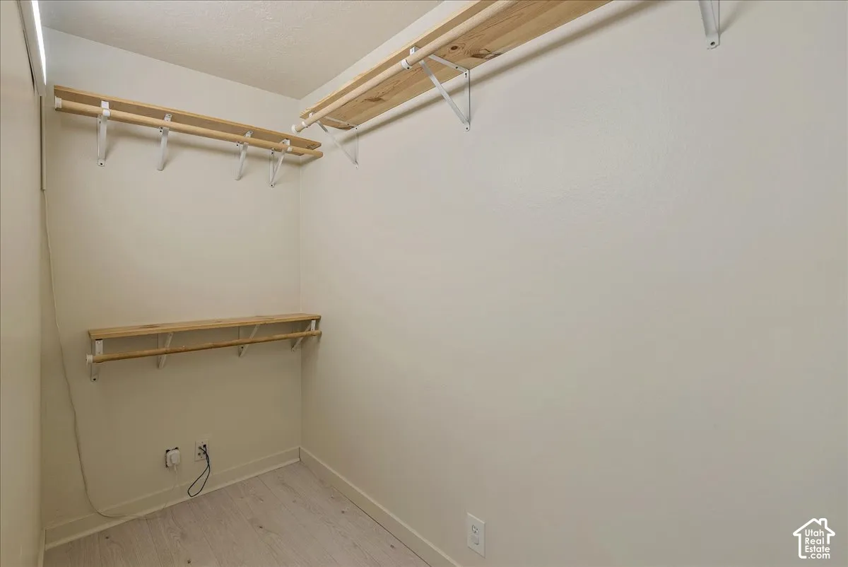 Storage space featuring multiple tiers of wall-mounted wood shelving and integrated rods, finished with wood-finish flooring