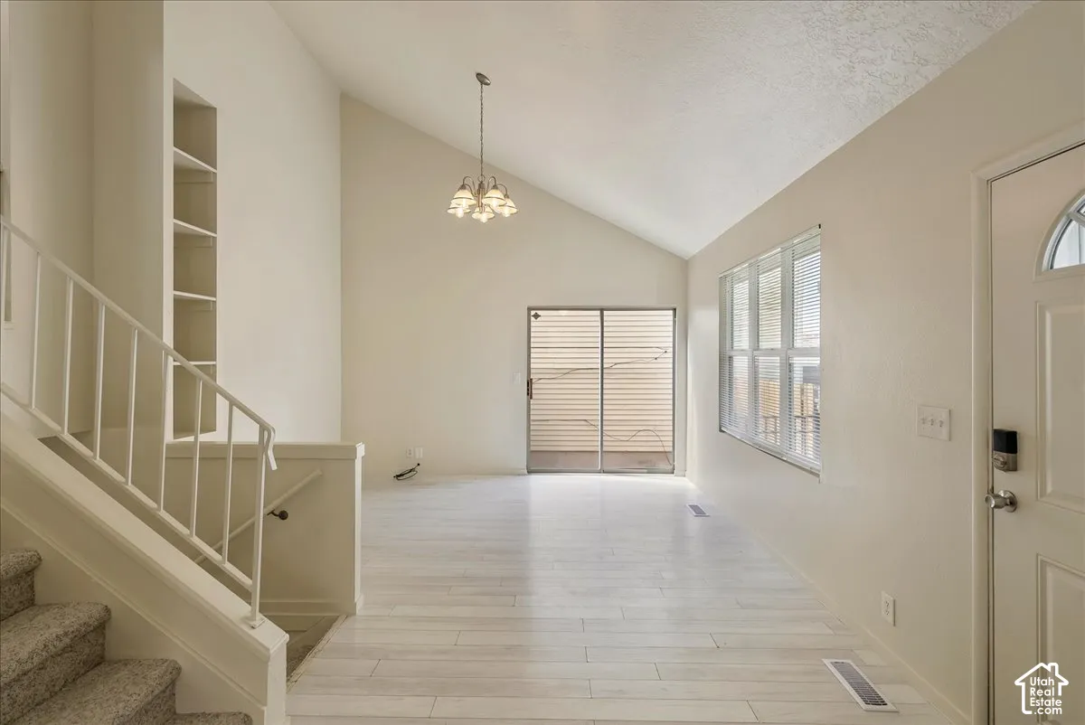 Vaulted ceilings, wood-finish flooring, recessed shelving, multi-light chandelier, and glass sliding door