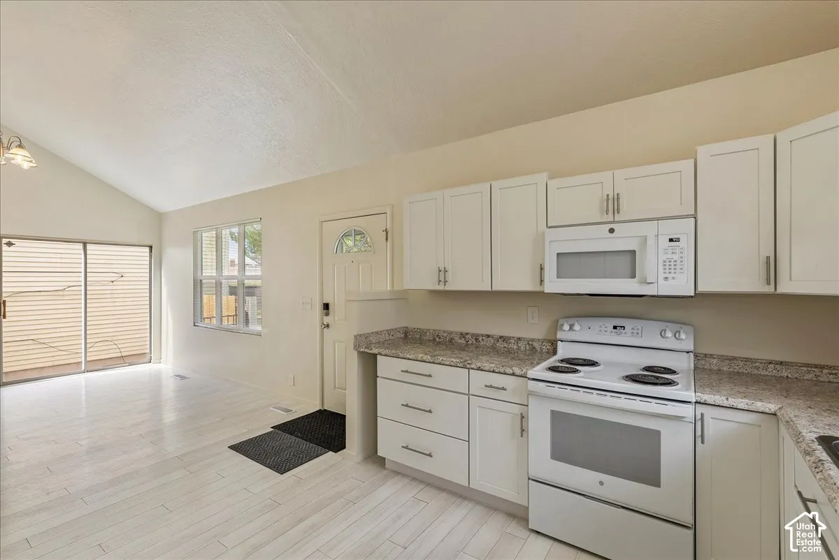 Kitchen featuring white cabinetry, stone-finish countertops, an over-the-range microwave, a white electric range, and wood-finish flooring under a vaulted ceiling