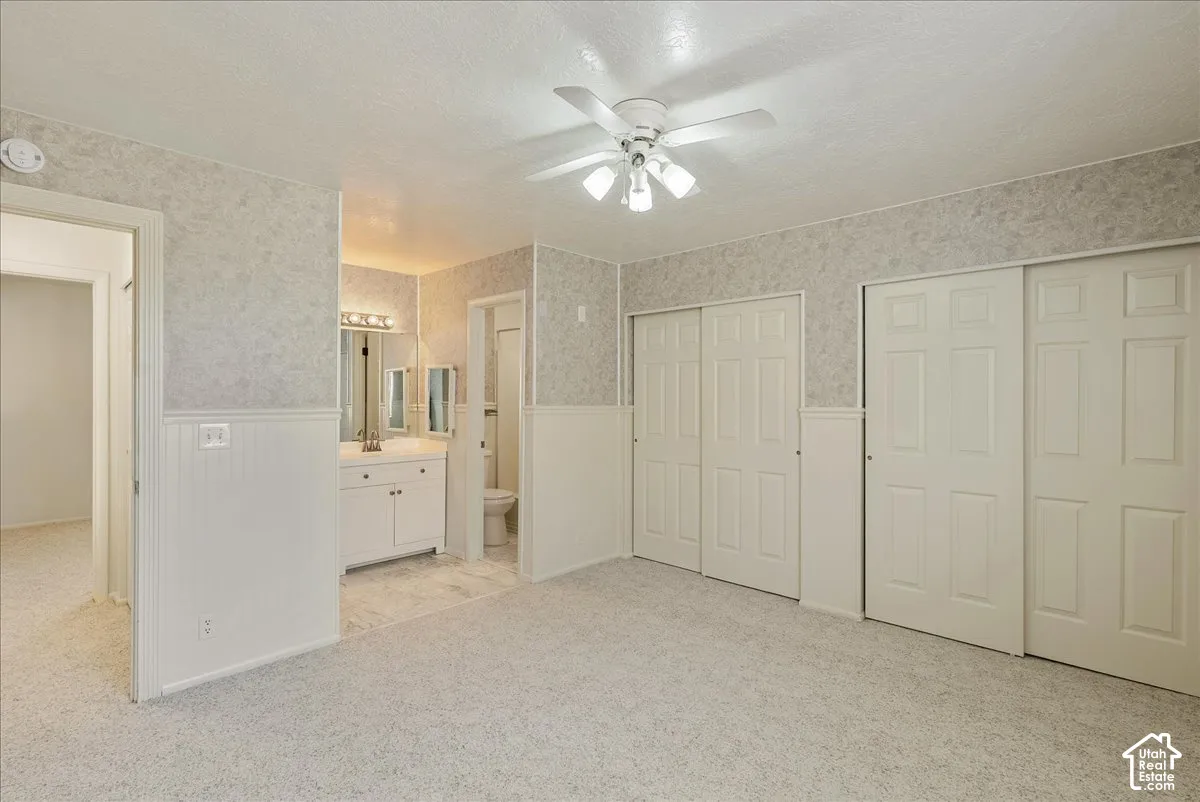 Room featuring neutral carpeting, wainscoting, dual sliding-panel closets, and an attached vanity area with an overhead multi-light fixture