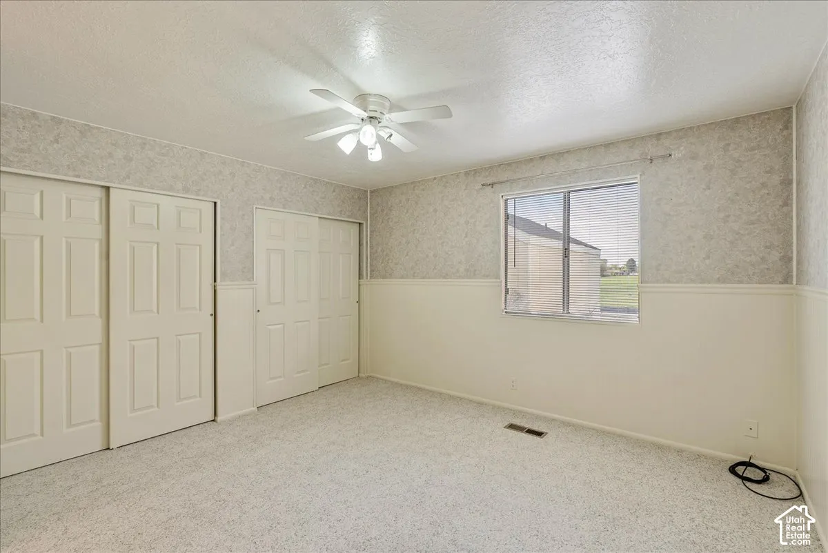 Interior space featuring carpeting, dual sets of closet doors, wall-mounted ceiling fan with light fixture, and horizontal window with blinds