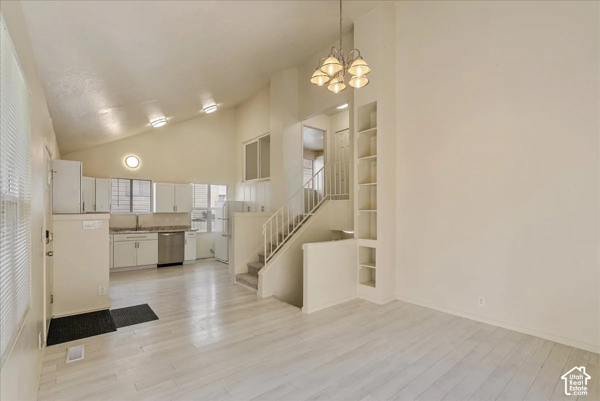 Open-concept interior featuring vaulted ceilings, wood-finish flooring, built-in floor-to-ceiling shelving, and a hanging multi-arm chandelier