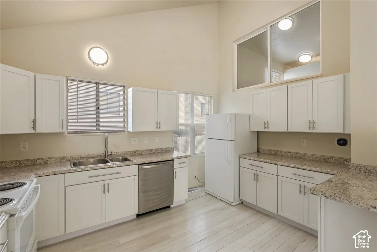 Kitchen featuring vaulted ceilings, white cabinetry, stone-finish countertops, stainless steel dishwasher, and wood-finish flooring
