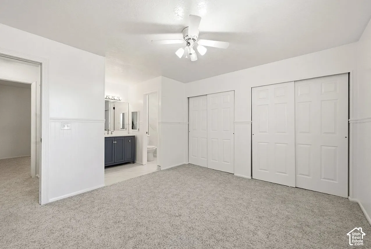 Neutral-toned carpet flooring, two double-panel sliding closets, integrated ceiling fan with light fixture, and beadboard wall paneling