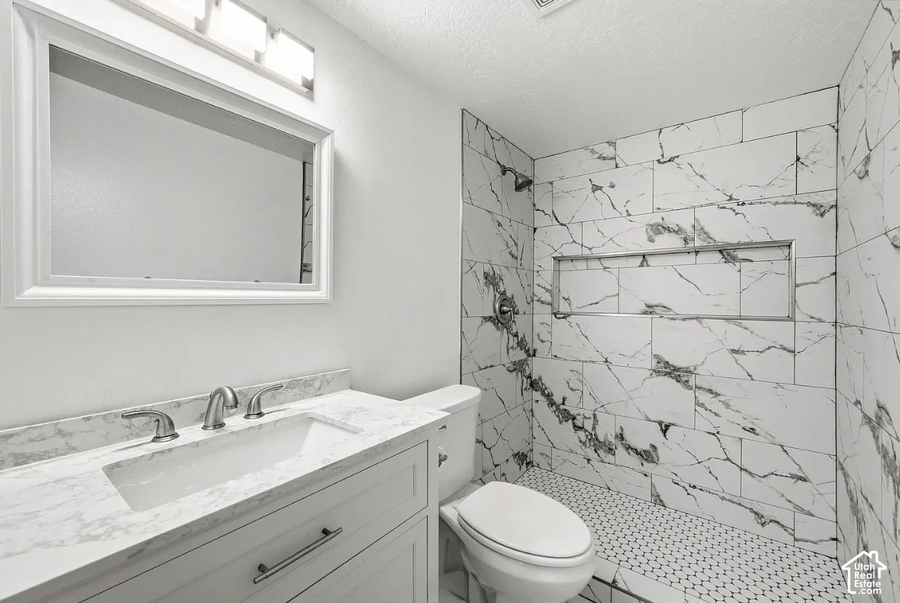 Bathroom featuring a vanity with stone-finish countertop, undermount sink, built-in shower niche, large-format tile shower surround, and a framed vanity mirror with integrated lighting