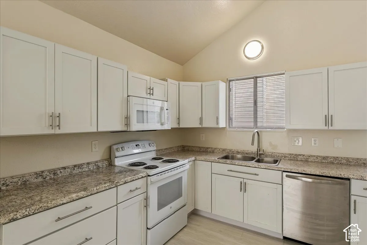 Kitchen featuring white cabinetry, stone-finish countertops, stainless steel dishwasher, vaulted ceiling, and dual-basin sink with a gooseneck faucet