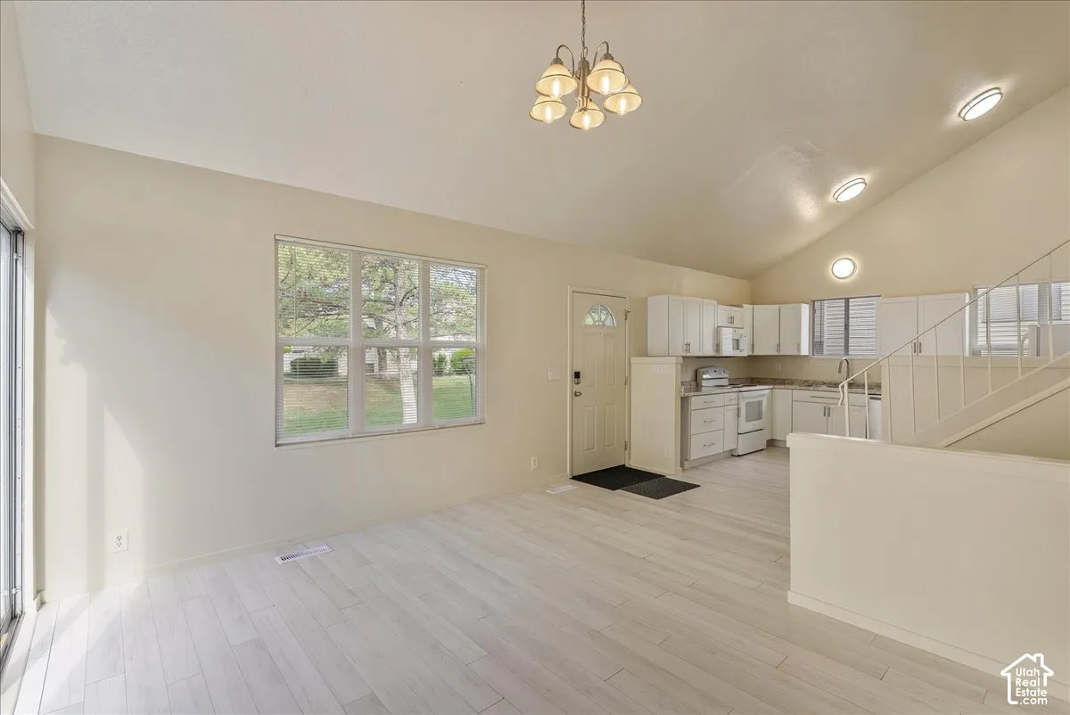 Vaulted ceilings, light-toned wood-finish flooring, white kitchen cabinetry, recessed lighting, and a multi-light chandelier