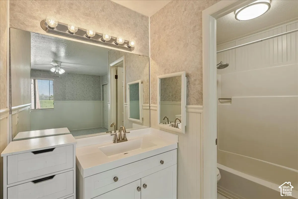 Bathroom featuring a white vanity cabinet with an integrated rectangular sink, brushed metal faucet, large wall-mounted mirror, and a shower-tub combination with white wall paneling