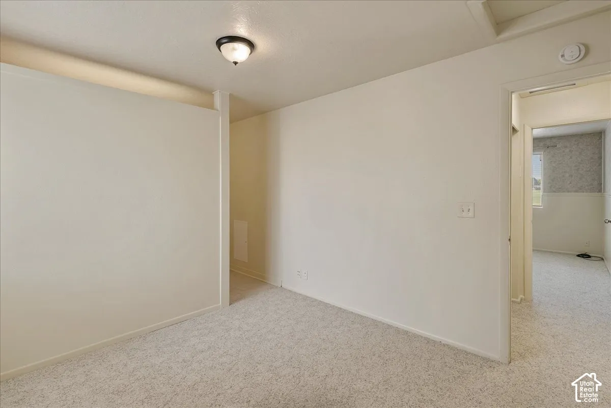 Neutral-toned interior space featuring wall-to-wall carpeting, a half-wall partition, and a flush-mount ceiling light fixture