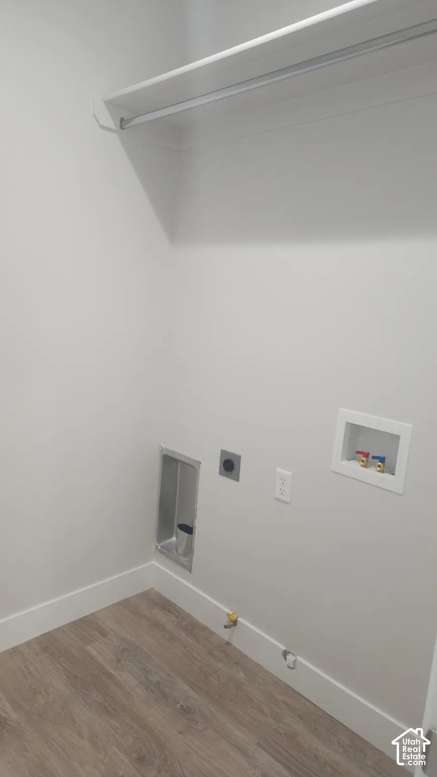 Laundry area featuring wood-finish flooring, a wall-mounted shelving unit, and recessed plumbing connections