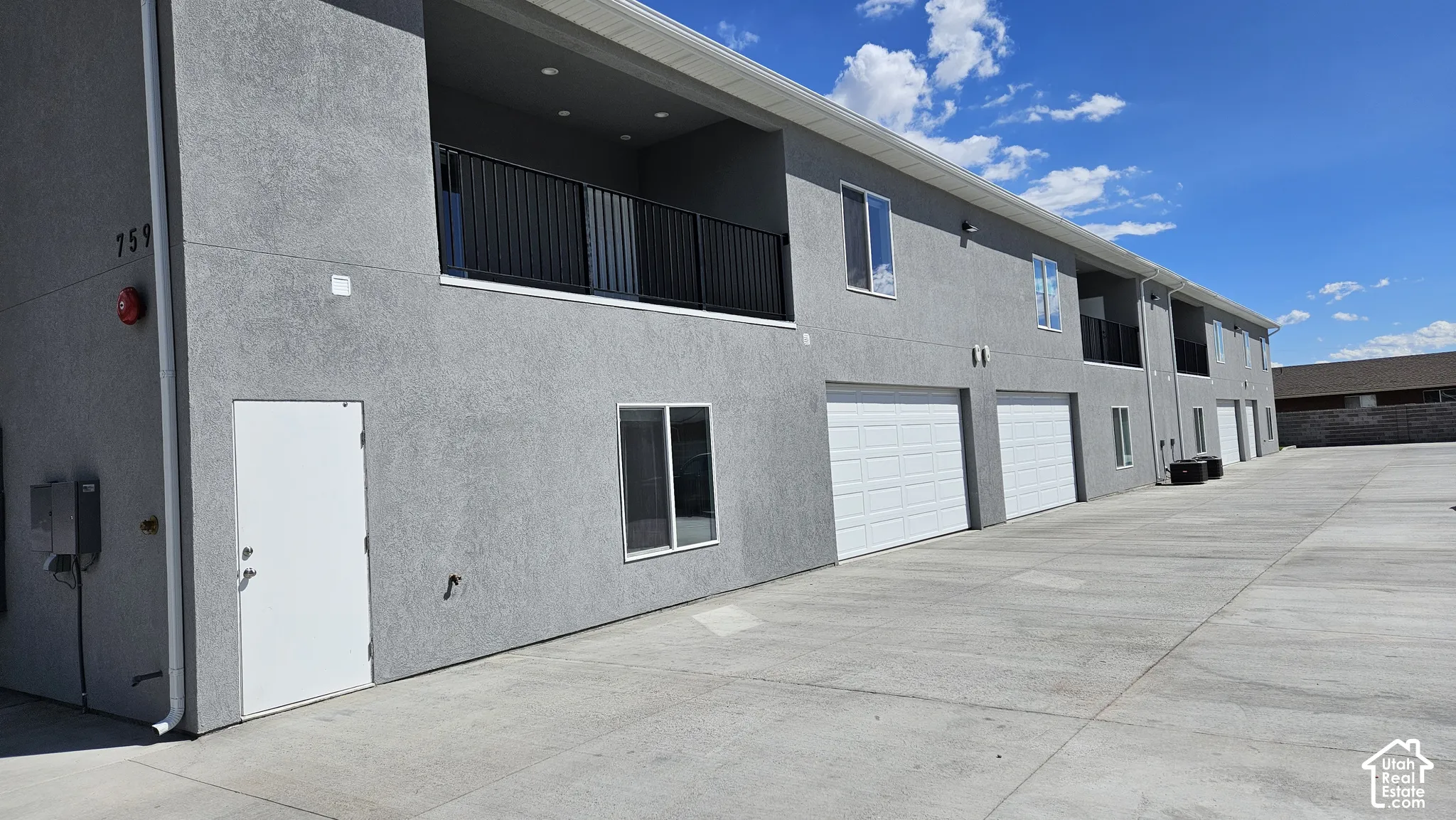 Multi-story stucco exterior featuring covered balconies with black metal railings, white sectional garage doors, and a concrete driveway
