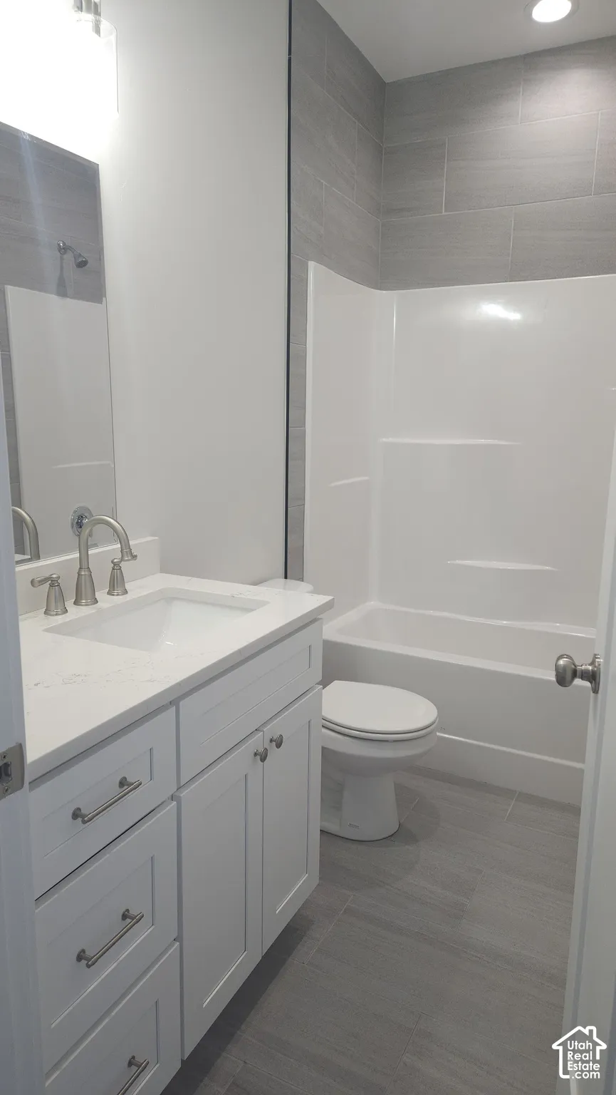 White cabinetry with brushed nickel hardware, light-toned quartz countertop with an integrated basin, brushed nickel widespread faucet, and grey tile flooring with matching wall tile surround in the tub area