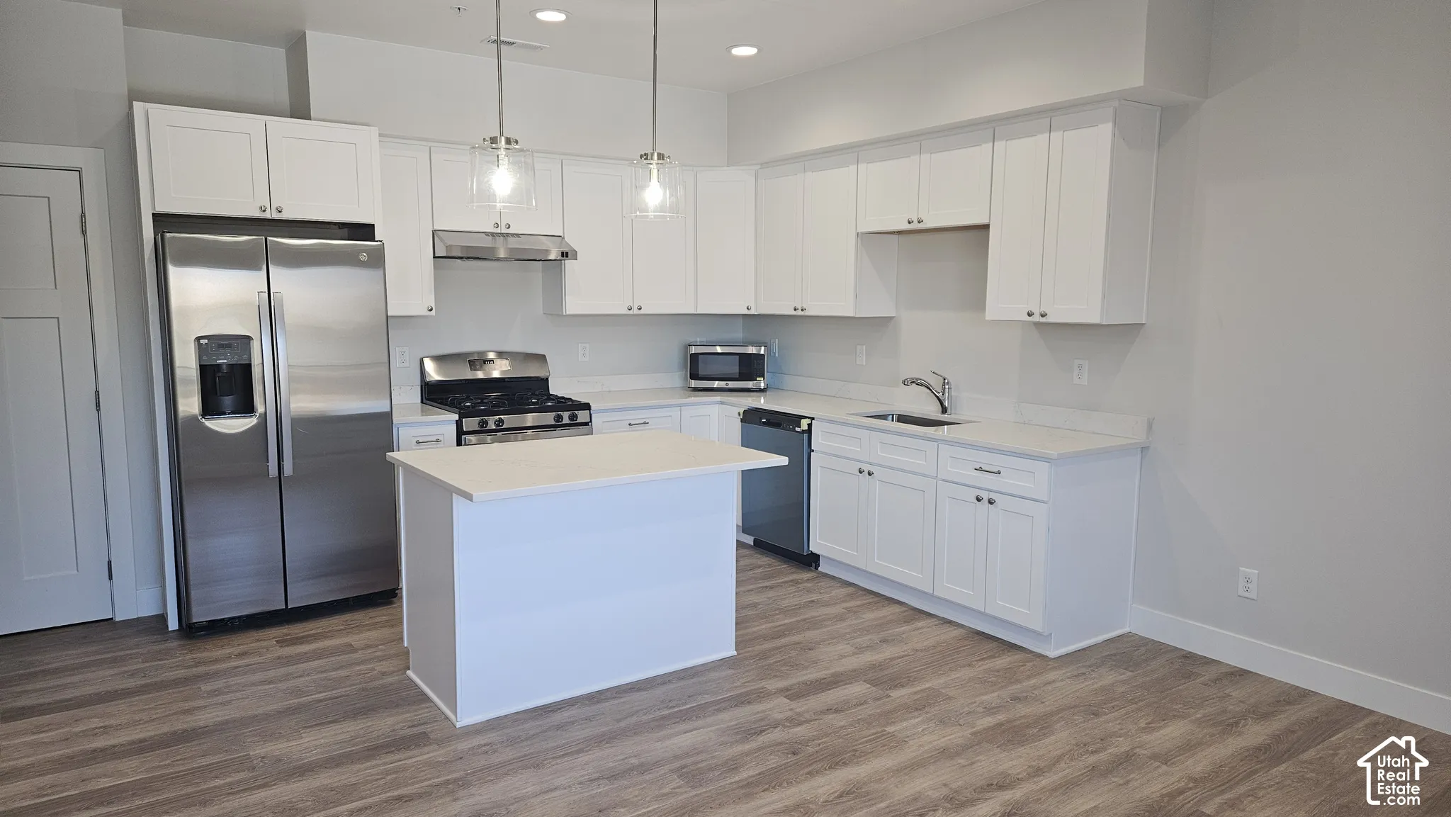 Kitchen featuring white cabinetry, solid-surface countertops, wood-finish flooring, stainless steel appliances, and dual pendant lighting