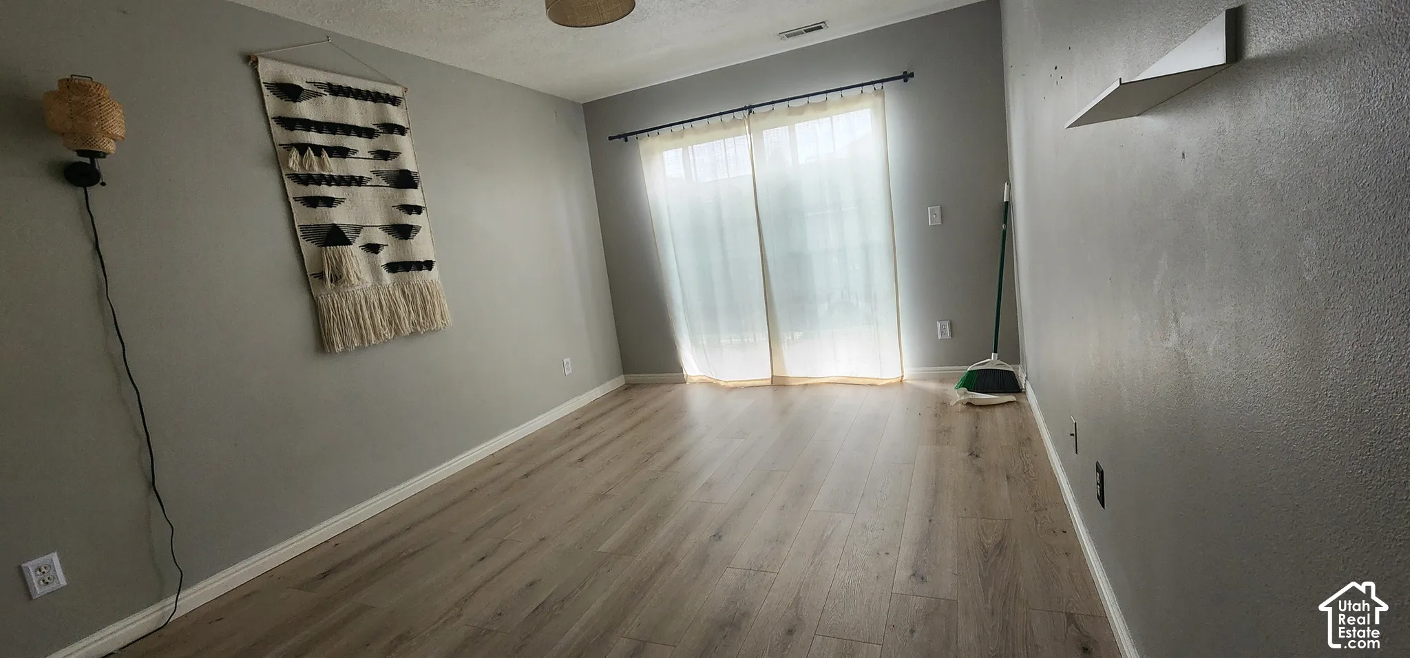 Wood-finish flooring, neutral-toned walls, and sliding glass door with a mounted curtain rod and wall-mounted shelving