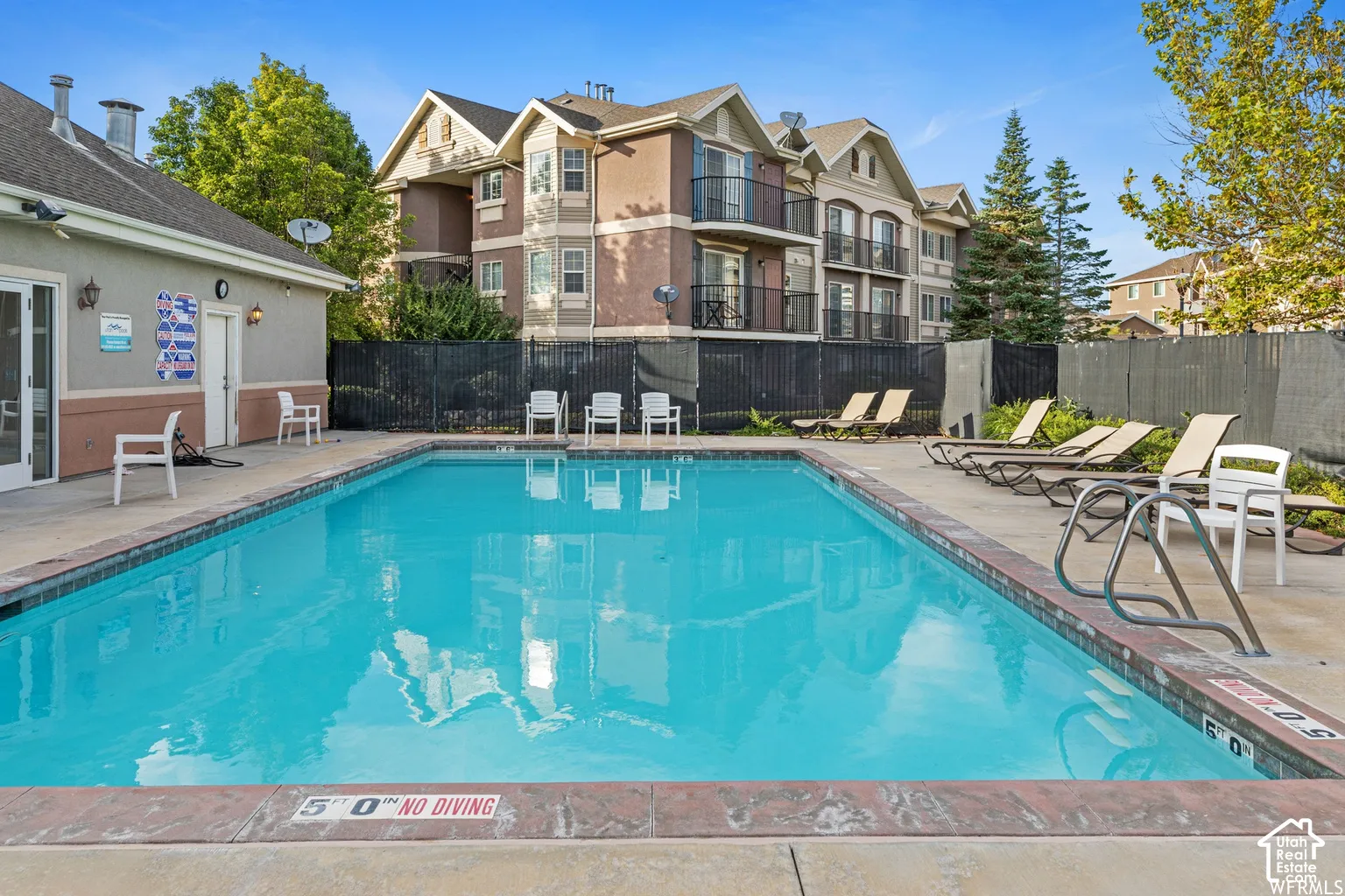 Outdoor swimming pool featuring a concrete deck, tile coping, metal handrails, and surrounding privacy fencing