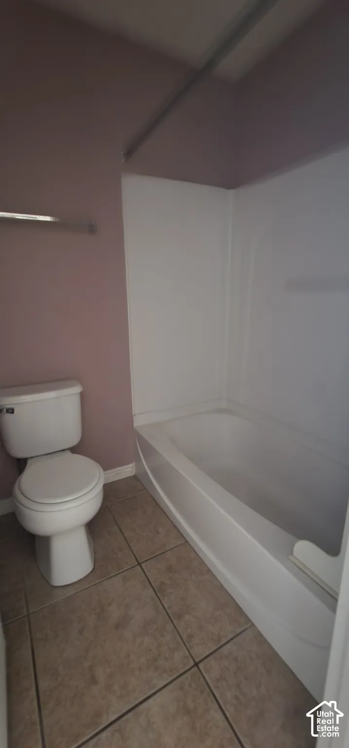 Bathroom featuring a composite bathtub and shower surround, ceramic tile flooring, and a porcelain toilet