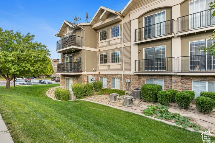 Multi-story residential exterior featuring stone masonry cladding at the base, upper-level balconies with black metal railings, and dual-pane windows with horizontal grid patterns