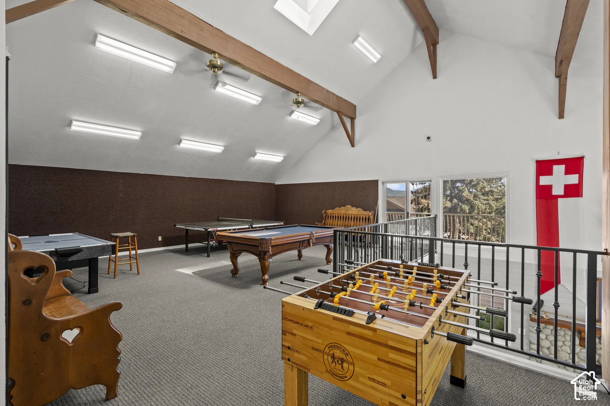 Vaulted ceiling featuring exposed wood-finish beams, recessed skylights, linear surface-mounted lighting, and iron balustrades