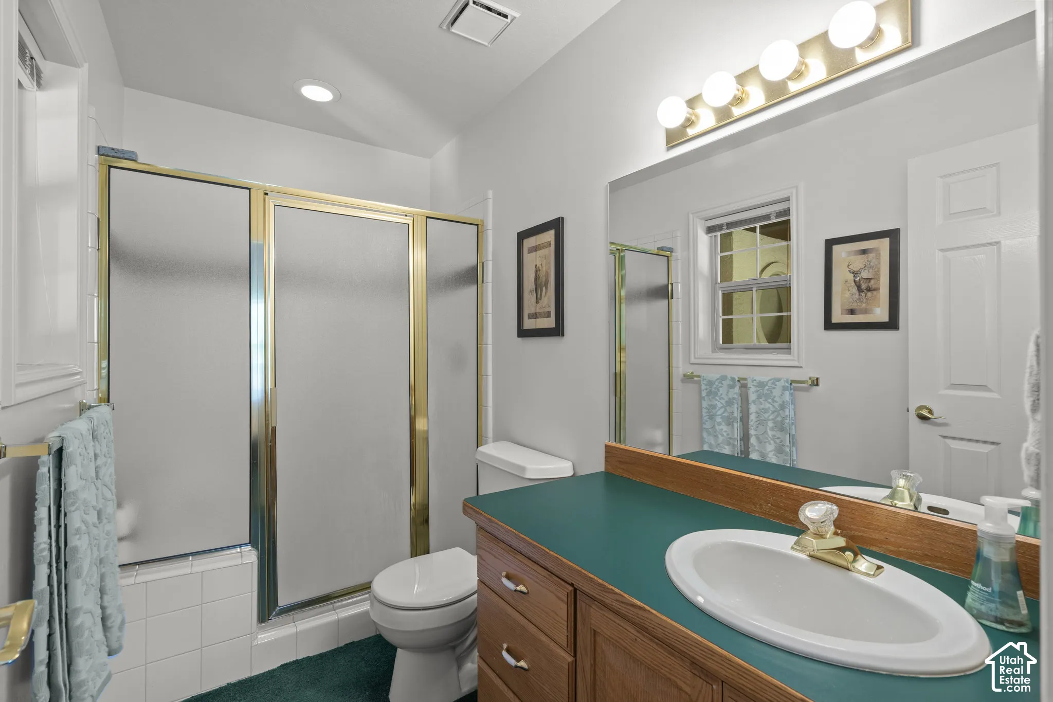 Bathroom featuring a vanity with wood cabinetry, a solid-surface countertop, an oval under-mount sink, and a walk-in shower with glass-paneled doors