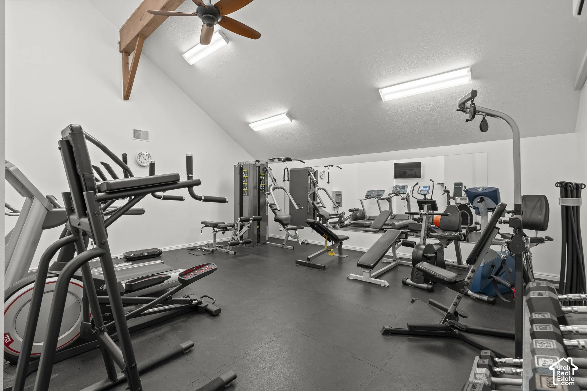 Vaulted ceiling with exposed wood beam, wall-to-wall mirror, rubber flooring, and multiple ceiling-mounted light fixtures