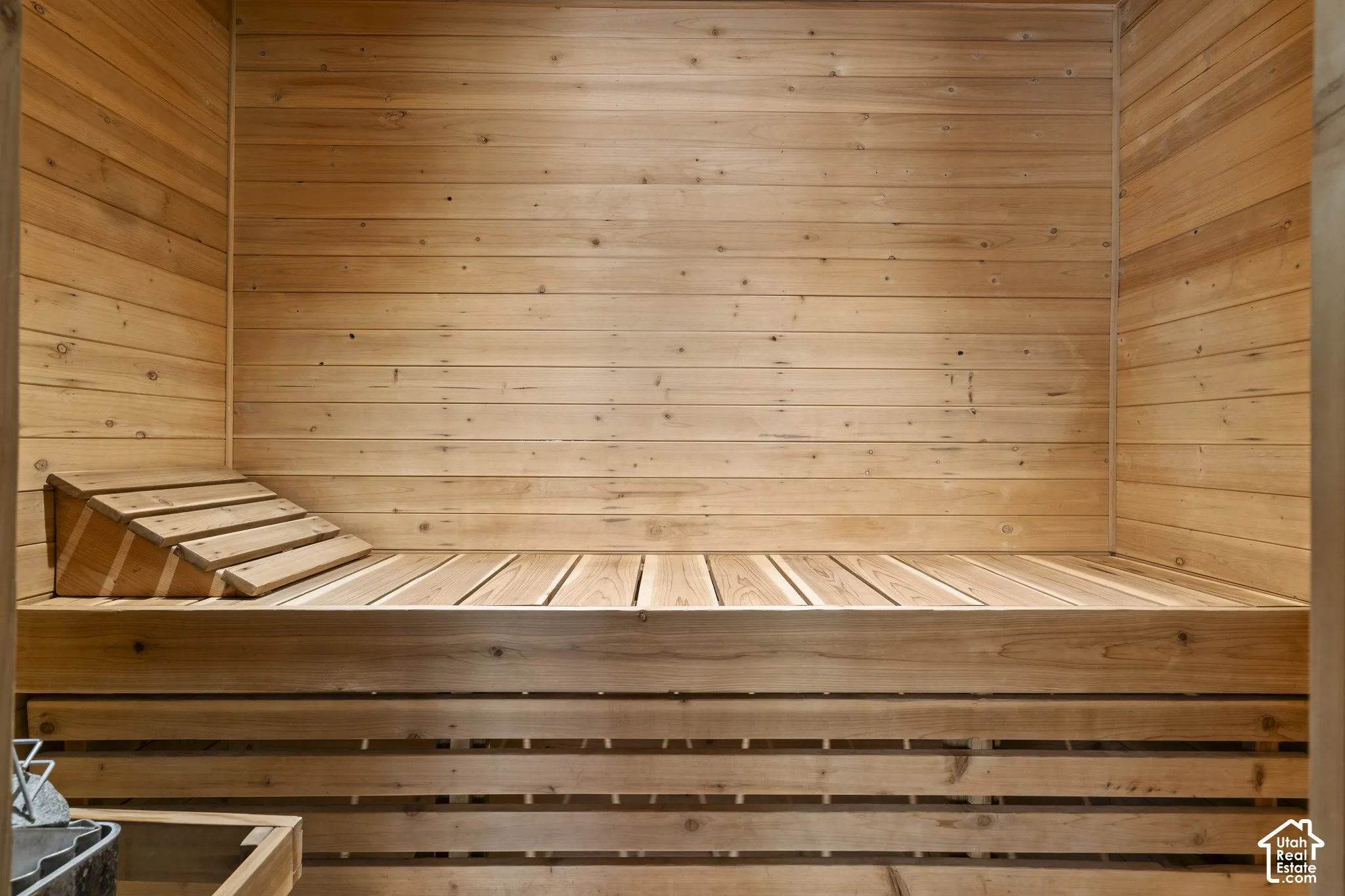 Sauna interior featuring natural wood wall paneling, built-in tiered wooden bench seating, and an integrated sloped wooden headrest