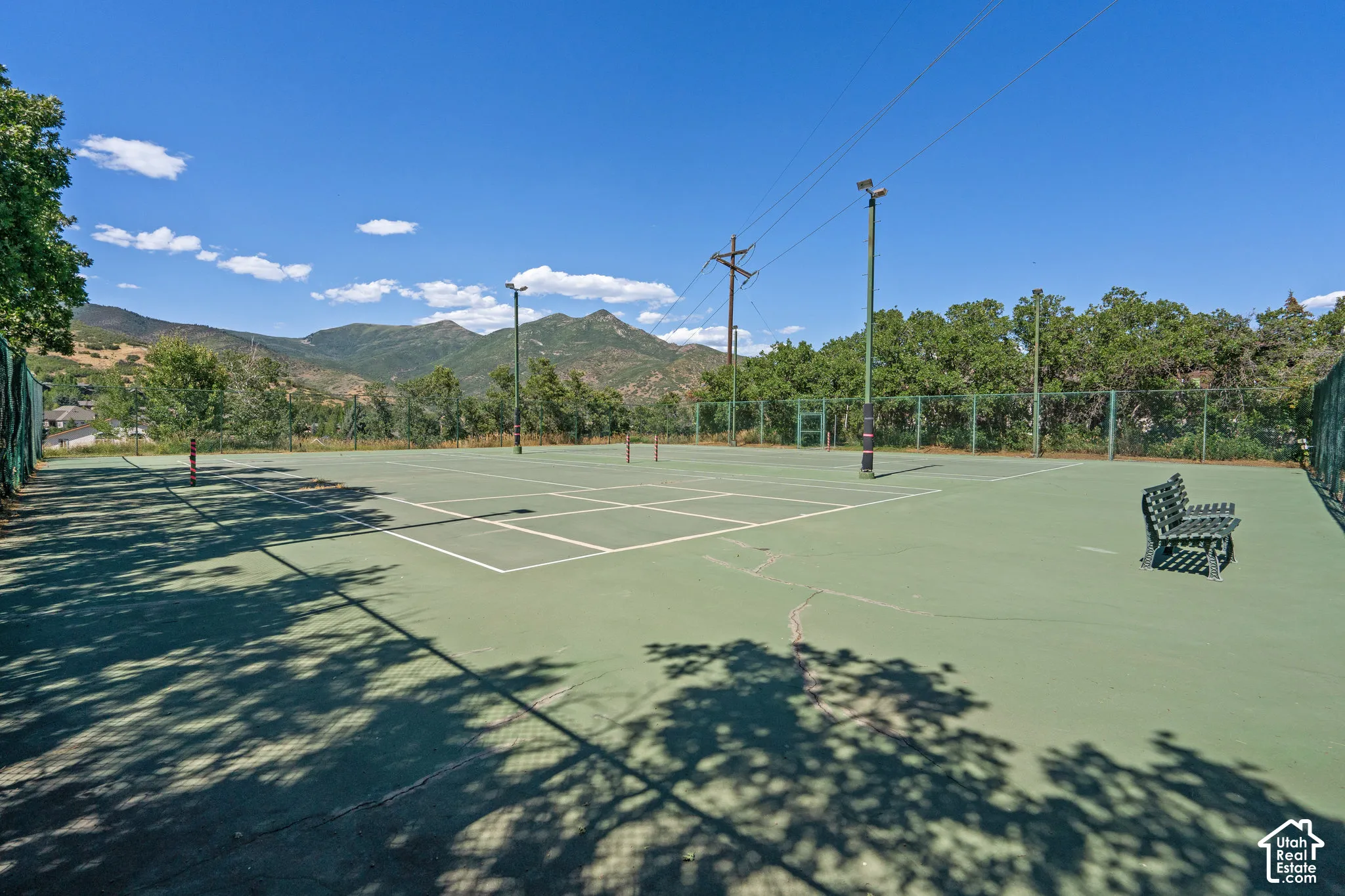 Tennis court with perimeter fencing, floodlight poles, and mountain backdrop
