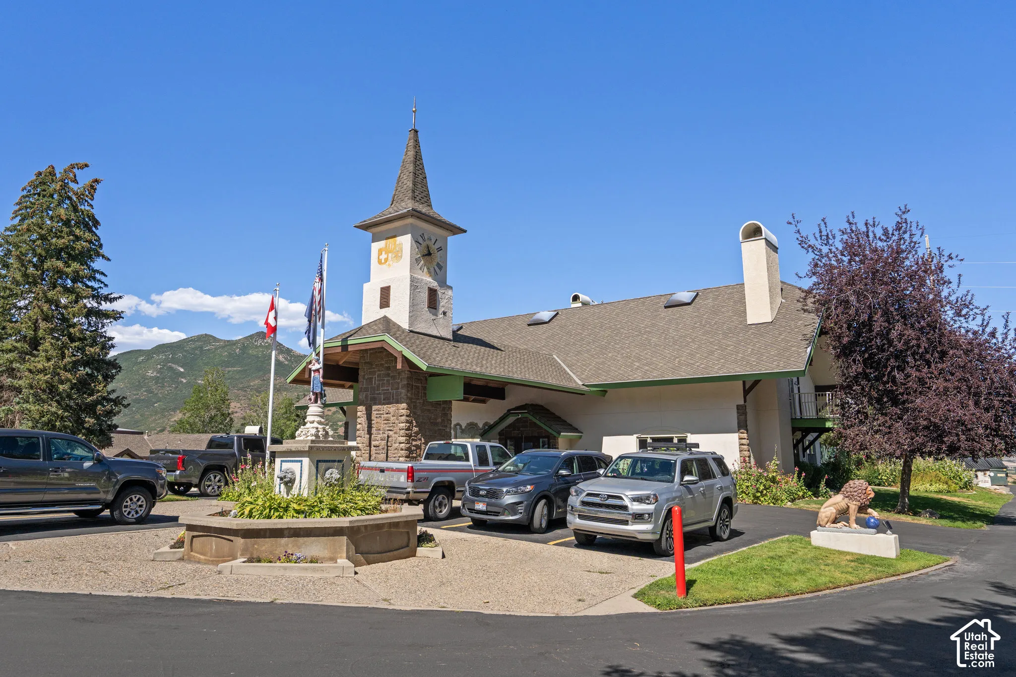 Exterior featuring a multi-story clock tower, stone masonry facade, asphalt shingle roofing, multiple skylights, and a decorative circular fountain