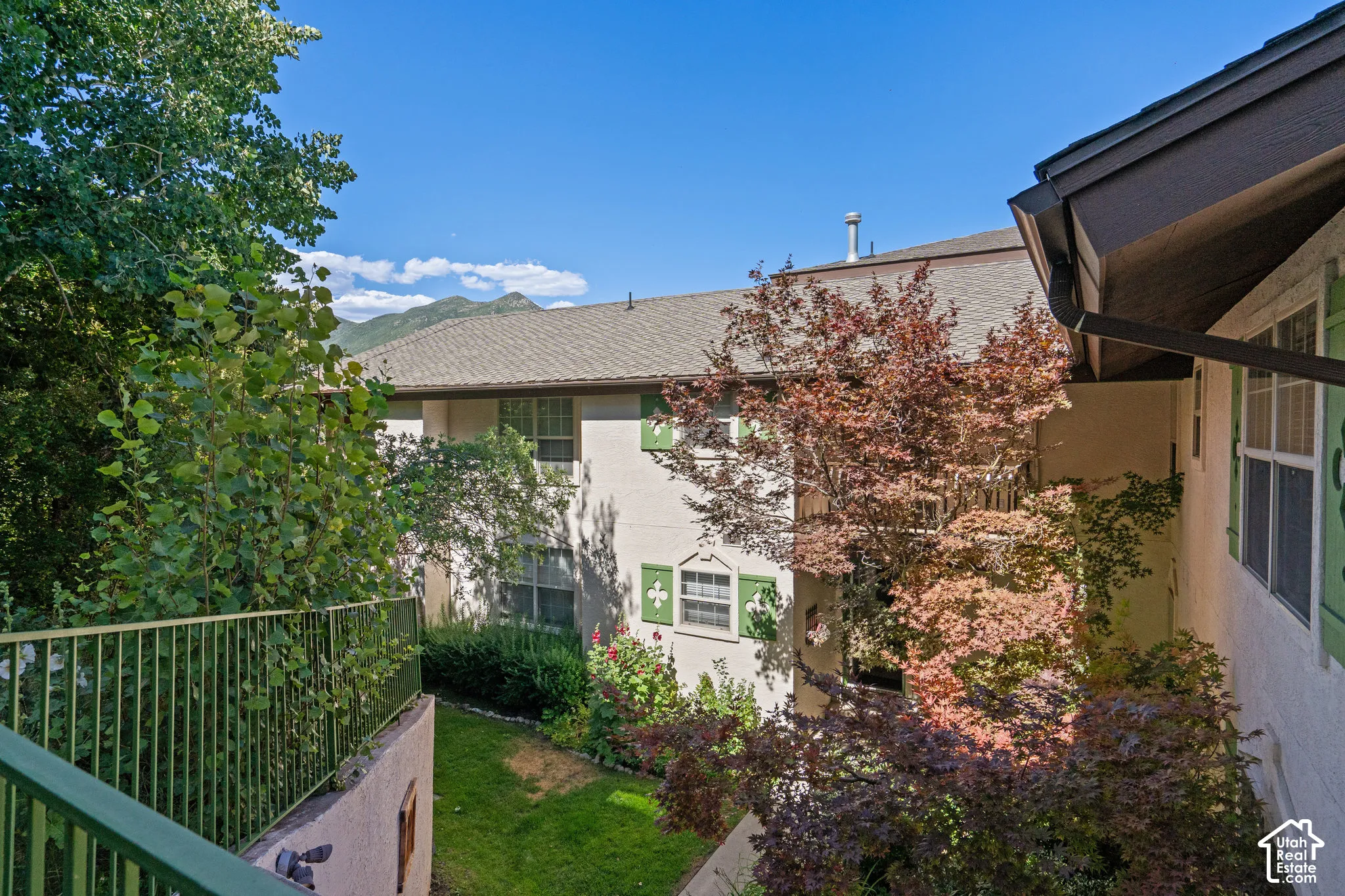 Stucco exterior with decorative shutters, integrated balcony featuring metal railings, mature landscaping, and mountain scenery