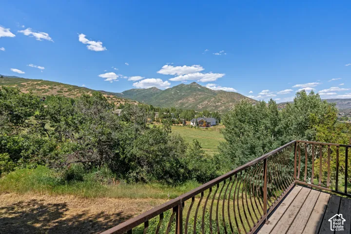 Elevated deck featuring metal railing, overlooking a sprawling landscape of mature trees, expansive greenery, and prominent mountain peaks