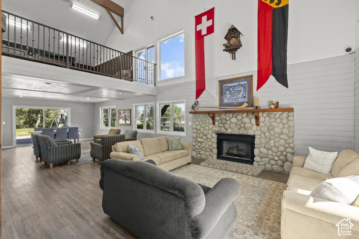 Vaulted ceiling featuring exposed timber beams, stone fireplace with a wood mantel, upper-level mezzanine, and wood-finish flooring