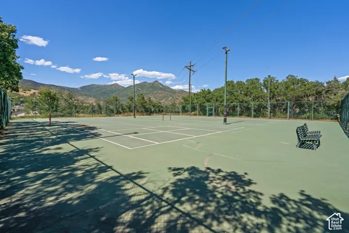 Tennis court with perimeter fencing, floodlight poles, and mountain backdrop