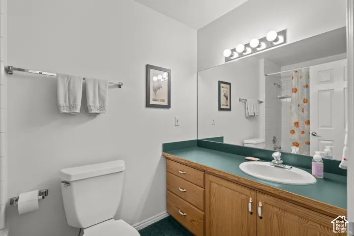 Full-width vanity featuring wood-finish cabinetry, solid-surface countertop with integrated backsplash, oval undermount sink, and expansive wall-to-wall mirror with four-light fixture