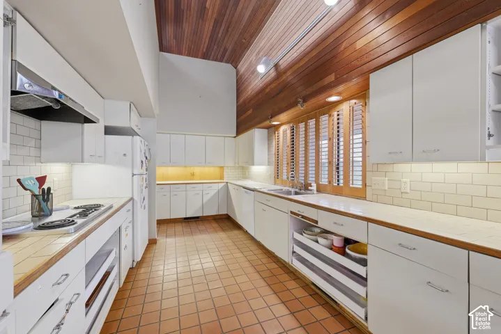 Kitchen featuring vaulted ceilings with wood-plank paneling, subway tile backsplash, white cabinetry, tile countertops, and ceramic tile flooring