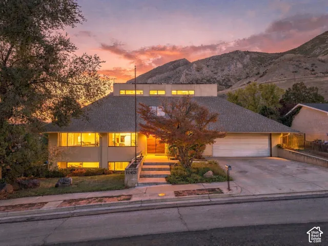 Contemporary exterior featuring stacked stone masonry, horizontal clerestory windows, an attached two-car garage, and concrete hardscaping against a mountain backdrop