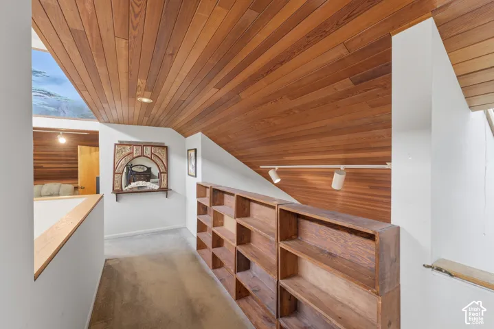 Vaulted ceiling with wood-plank paneling, integrated track lighting, custom built-in wood shelving, and skylight