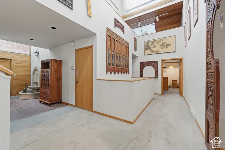 Interior hallway featuring high ceilings with integrated skylights, wood-plank ceiling accents, a stone water feature, and tile flooring