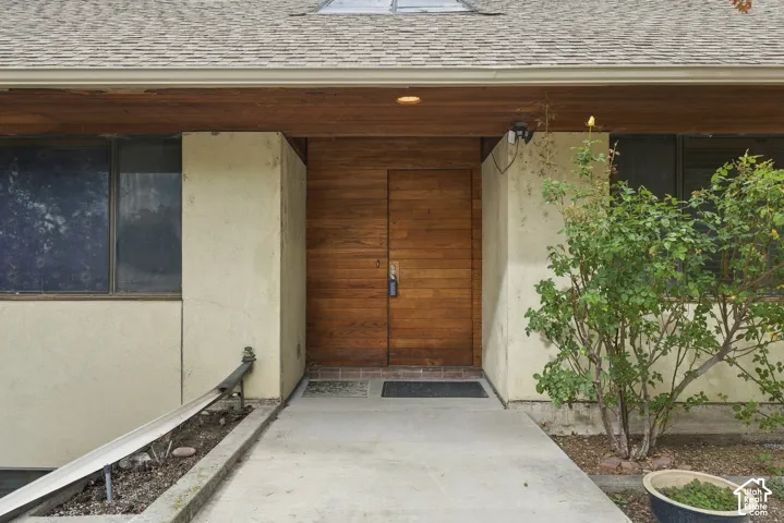 Mid-century architectural exterior featuring a natural wood-finish horizontal plank entry door, wood-paneled soffit, recessed lighting, and stucco siding
