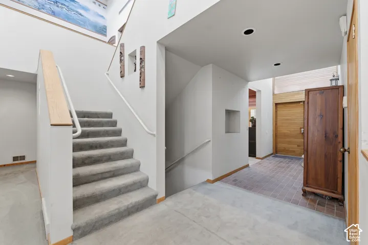 Staircase with wood-finish handrail, recessed wall niches, entryway featuring brick-style tile flooring, and integrated ceiling lighting