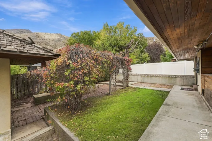 Outdoor space featuring a concrete patio, brick walkway, wood-plank soffit, pergola, and mountain backdrop