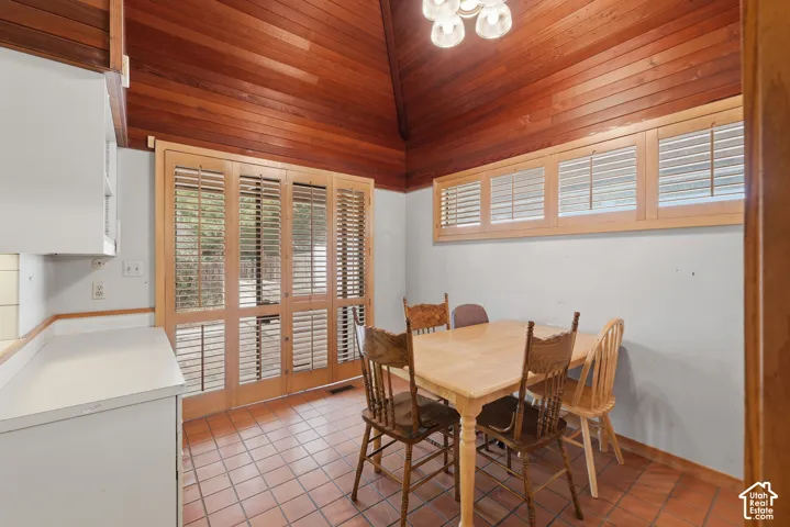 Vaulted wood-plank ceiling, terra cotta tile flooring, light-toned wood-framed glass patio doors, and matching wood-frame window shutters