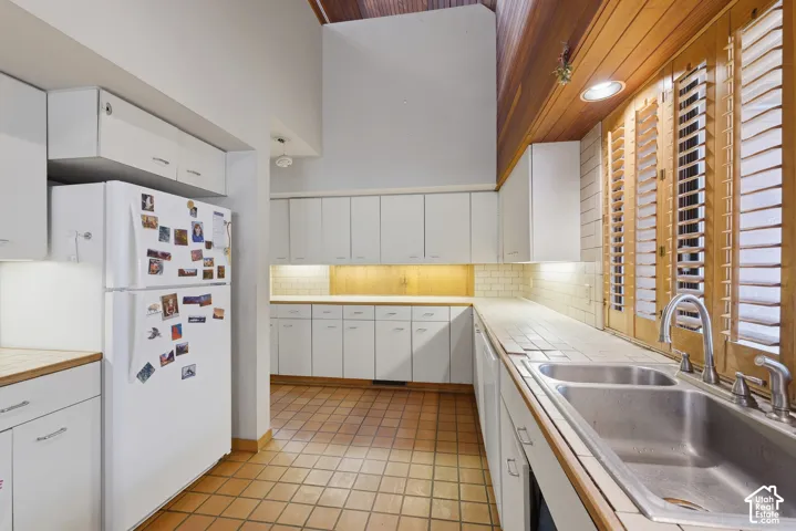 Kitchen featuring white cabinetry, vaulted ceilings with wood-plank detailing, tile flooring, ceramic tile backsplash, and a dual-basin stainless steel sink