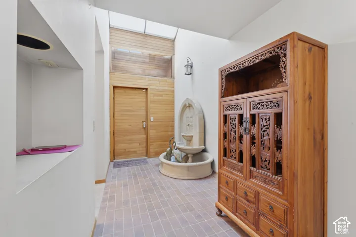 Atrium entrance featuring a skylight, stone fountain, wood-paneled accent wall, and tiled flooring